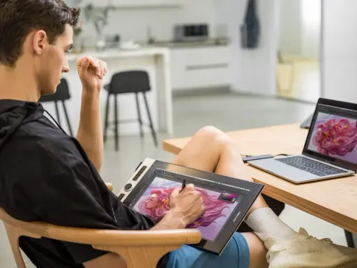 Un jeune homme utilise une tablette graphique pour créer une œuvre d'art numérique, sa configuration PC graphiste est prête pour l'inspiration.