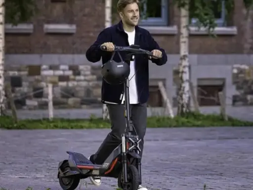 Un homme souriant sur une trottinette électrique puissante, dépassant les 25 km/h. La réglementation sur ces engins est à considérer.
