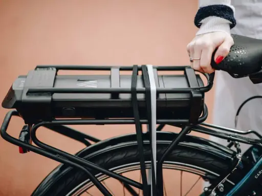Main d'une femme tenant la selle d'un vélo électrique, avec la batterie visible sur le porte-bagages. Idéal pour tester la batterie du vélo.