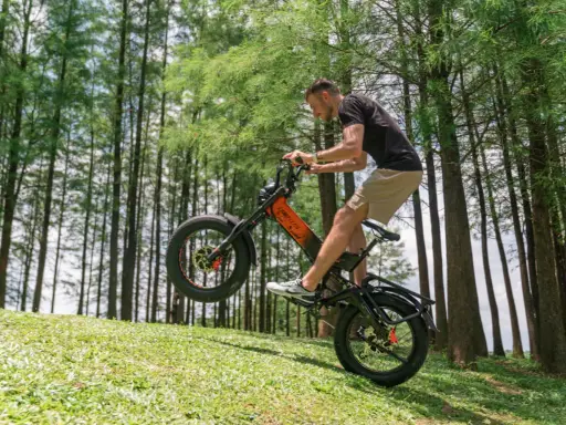 Un homme fait du vélo électrique en montée, le pneu avant décollé du sol. Il semble s'amuser, explorant quelle vitesse pour monter une côte en vélo électrique.