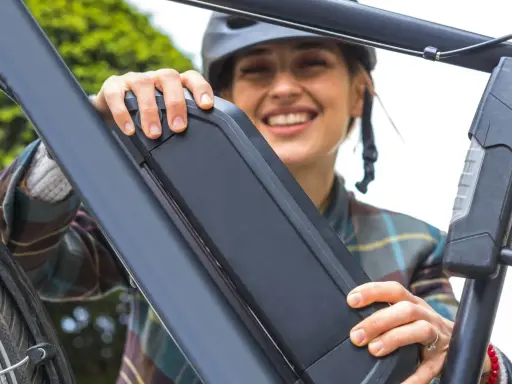 Une femme souriante manipule la batterie de son vélo électrique, peut-être pour apprendre comment réinitialiser une batterie de vélo électrique.