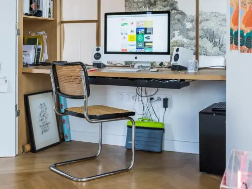 Bureau moderne avec iMac, chaise en rotin et étagères. Idéal pour savoir comment choisir un ordinateur de bureau adapté à votre espace de travail.