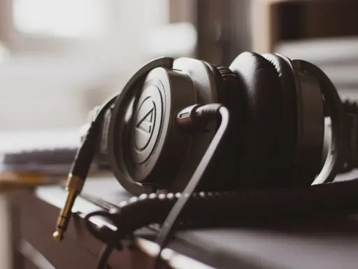 Gros plan sur un casque audio noir, avec son câble spiralé et sa prise jack dorée. La sensibilité du casque audio est palpable.