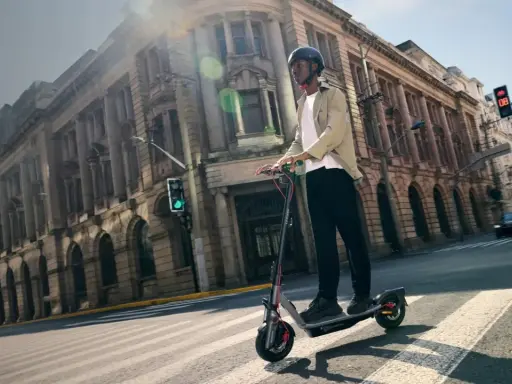 Un homme roule en trottinette électrique dans une rue bordée de bâtiments anciens. La taille roue trottinette semble adaptée à la ville.