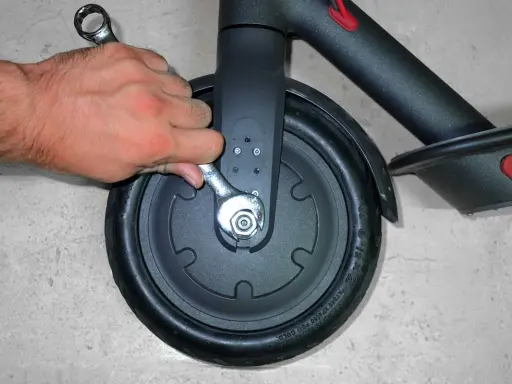 Main tenant utilise une clé pour changer la roue avant d'une trottinette électrique.