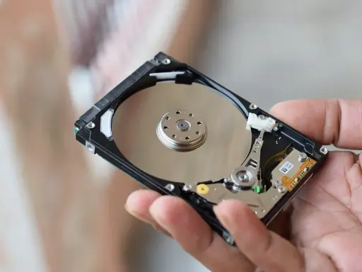Main d'une personne tenant un disque dur interne, montrant les plateaux réfléchissants et les composants électroniques. Il existe différents types de disques durs.