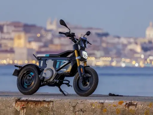 Une trottinette électrique BMW futuriste, aux lignes audacieuses, se dresse sur un quai, la ville illuminée en arrière-plan.