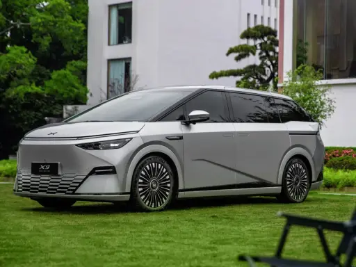 Le Xpeng X9, un monospace argenté futuriste, est garé sur une pelouse verte devant un bâtiment moderne.