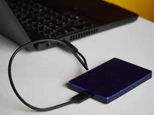 Un disque dur externe bleu est connecté à un ordinateur portable. Un guide pour comment choisir un disque dur.