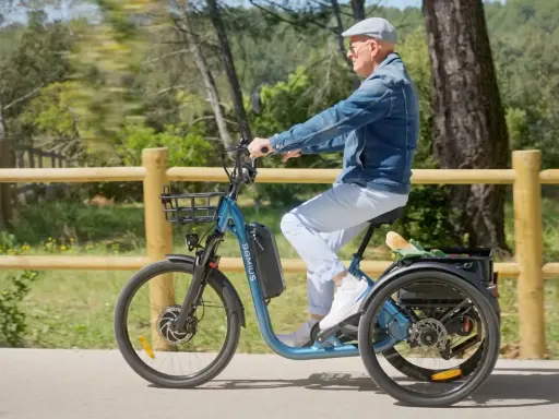 Un homme âgé roule sur un tricycle électrique bleu, son certificat d'homologation vélo électrique en poche.
