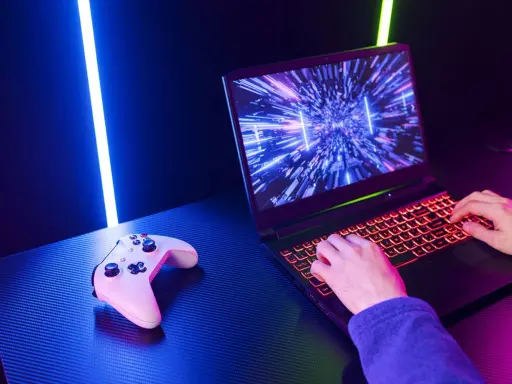 Un joueur utilise un PC portable gamer avec un clavier rétroéclairé. Une manette est posée à côté. Comment choisir son PC portable gamer ?