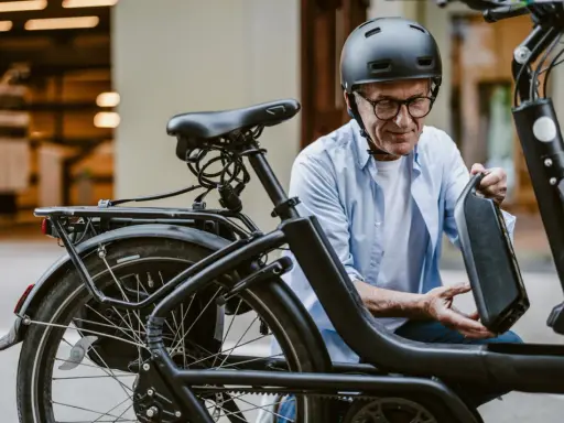 Un homme en casque retire la batterie de son vélo électrique, prêt pour l'immatriculation vélo électrique.