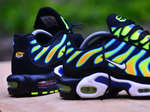 Paire de baskets Nike Air Max Plus TN, noires avec des vagues dégradées de jaune, orange et bleu.