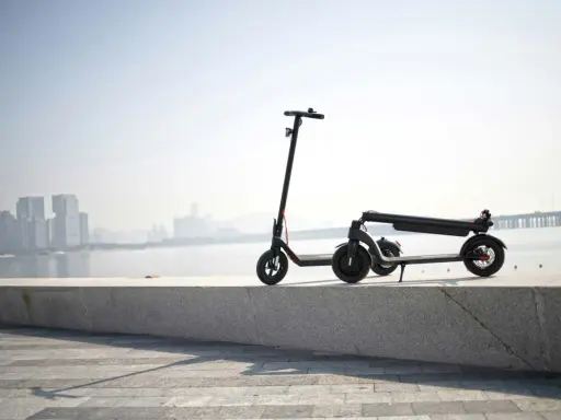 Une trottinette électrique s'allume mais ne bouge pas, posée sur un muret face à une ville et un pont.