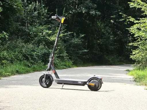 Trottinette Xiaomi grise sur une route asphaltée, entourée de verdure. Parfait pour explorer la nature et profiter de son autonomie.