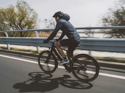 Un cycliste sur un vélo électrique qui se recharge en roulant, longeant une voie rapide bordée d'eau et d'arbres.