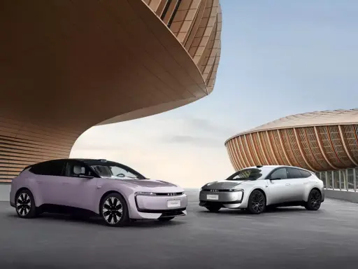 Deux Audi E5 Sportback, une lilas et une argentée, se présentent devant des bâtiments aux formes organiques.