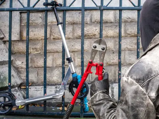 Un voleur, cagoulé et ganté, s'apprête à couper le cadenas d'une trottinette volée avec une pince monstre. Comment retrouver une trottinette volée ?