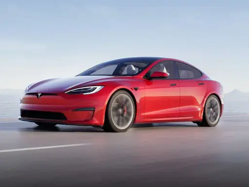 Une Tesla Model S Plaid rouge vif file sur une route côtière, le soleil se reflétant sur sa carrosserie élégante.