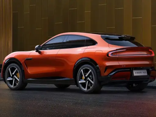 La **Xiaomi car** orange vif, un SUV coupé futuriste, se gare devant un bâtiment moderne aux reflets dorés.