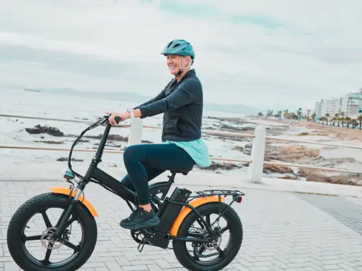 Une femme souriante roule sur un vélo électrique, profitant de la vue sur la mer. Le poid du vélo électrique ne l'empêche pas de profiter de sa balade.