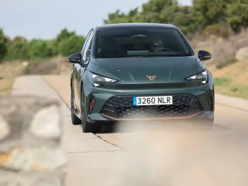 La Cupra Born VZ, d'un vert profond, roule sur une route de campagne. Un conducteur porte des lunettes de soleil.