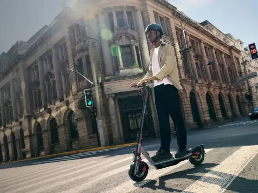 Un homme en casque roule sur la trottinette électrique la plus rapide du monde, traversant une rue bordée de bâtiments historiques.
