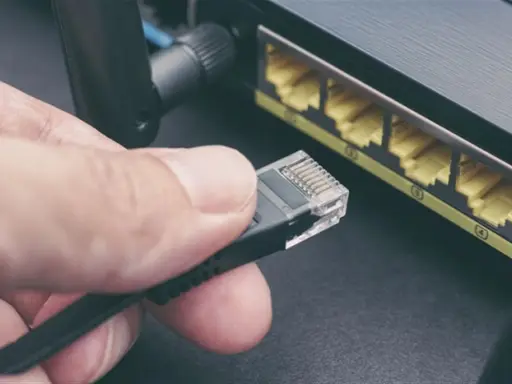 Maintenant, comment choisir son cable ethernet ? Une main tient un connecteur RJ45 près des ports d'un routeur.