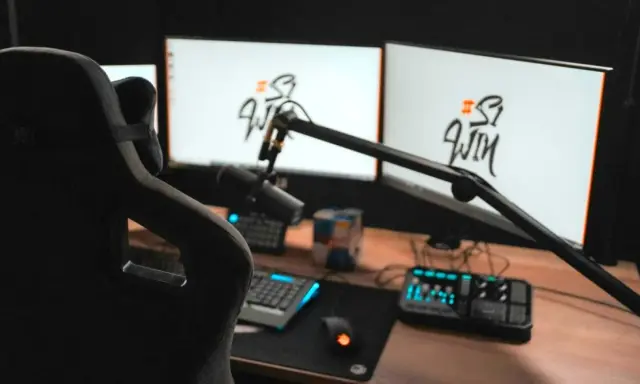 Setup streamer avec fauteuil, deux écrans affichant un logo, micro sur bras articulé, clavier, souris et console de mixage.