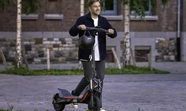 Un homme souriant sur une trottinette électrique puissante, dépassant les 25 km/h. La réglementation sur ces engins est à considérer.