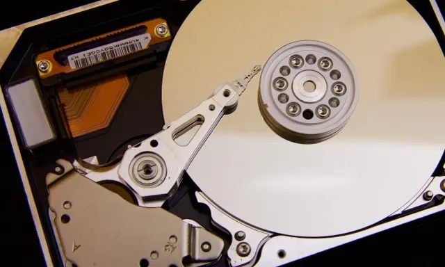 Vue rapprochée de l'intérieur d'un disque dur de PC, montrant le plateau, la tête de lecture/écriture et le moteur. L'emplacement du disque dur est essentiel pour le stockage des données.