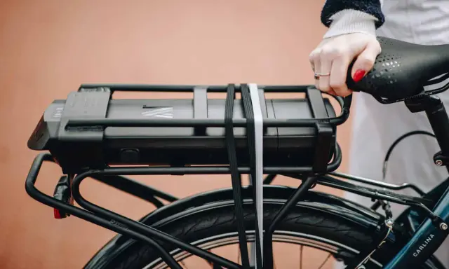 Main d'une femme tenant la selle d'un vélo électrique, avec la batterie visible sur le porte-bagages. Idéal pour tester la batterie du vélo.