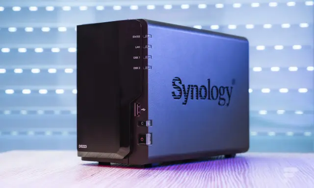 Un appareil Synology DS223, un nas stockage compact, est présenté sur un bureau en bois, avec un fond lumineux.
