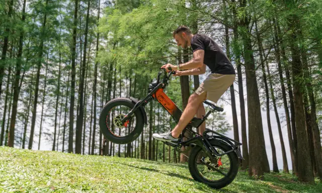 Un homme fait du vélo électrique en montée, le pneu avant décollé du sol. Il semble s'amuser, explorant quelle vitesse pour monter une côte en vélo électrique.