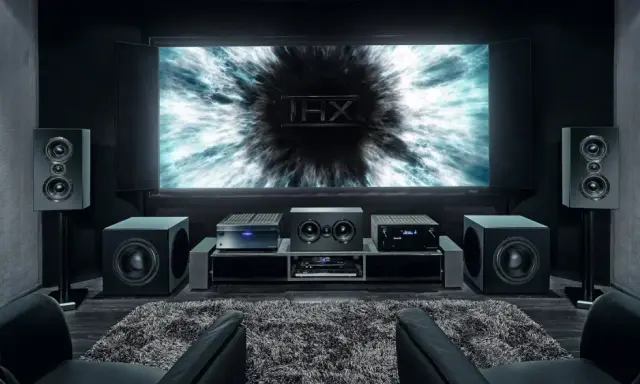 Installation home cinema avec écran THX, amplificateur, enceintes et fauteuils en cuir noir pour une expérience immersive.