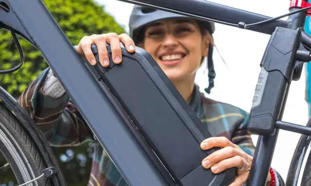 Une femme souriante manipule la batterie de son vélo électrique, peut-être pour apprendre comment réinitialiser une batterie de vélo électrique.