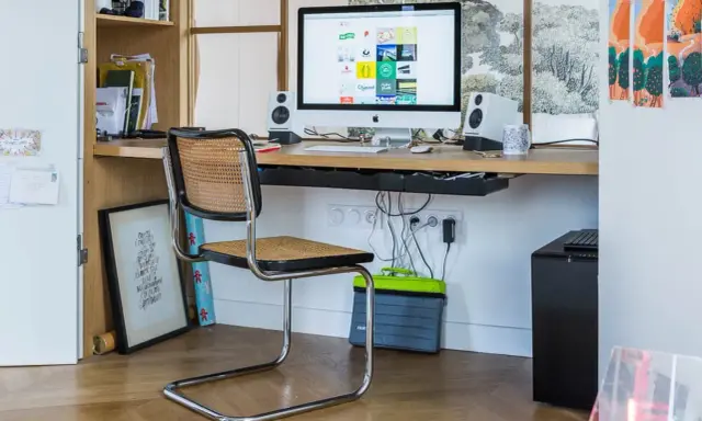 Bureau moderne avec iMac, chaise en rotin et étagères. Idéal pour savoir comment choisir un ordinateur de bureau adapté à votre espace de travail.