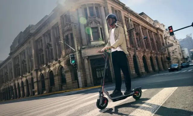 Un homme roule en trottinette électrique dans une rue bordée de bâtiments anciens. La taille roue trottinette semble adaptée à la ville.