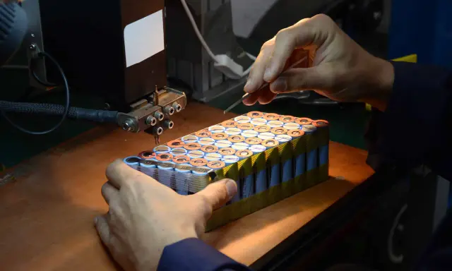 Un technicien assemble des cellules pour comment reparer une batterie de velo electrique. Il utilise un outil de soudure par points.