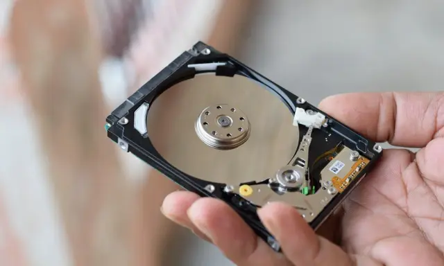 Main d'une personne tenant un disque dur interne, montrant les plateaux réfléchissants et les composants électroniques. Il existe différents types de disques durs.