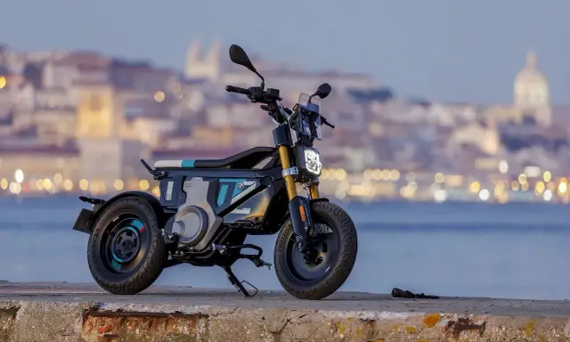 Une trottinette électrique BMW futuriste, aux lignes audacieuses, se dresse sur un quai, la ville illuminée en arrière-plan.