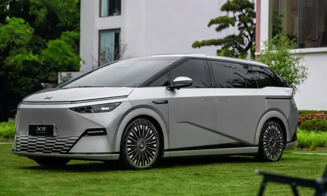Le Xpeng X9, un monospace argenté futuriste, est garé sur une pelouse verte devant un bâtiment moderne.