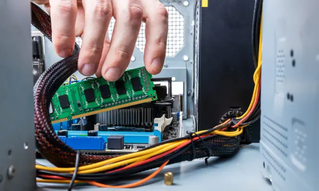 Main d'un homme insérant une barrette de RAM verte dans un emplacement de carte mère. Guide pour comment installer RAM.