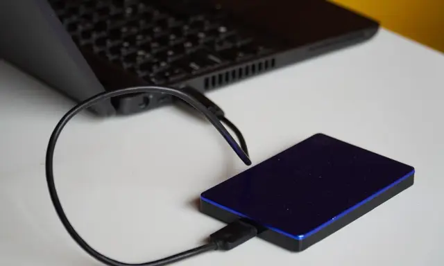 Un disque dur externe bleu est connecté à un ordinateur portable. Un guide pour comment choisir un disque dur.
