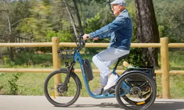 Un homme âgé roule sur un tricycle électrique bleu, son certificat d'homologation vélo électrique en poche.