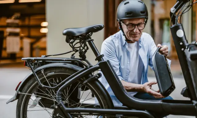 Un homme en casque retire la batterie de son vélo électrique, prêt pour l'immatriculation vélo électrique.