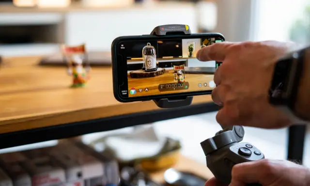 Main tenant, une main utilise un stabilisateur pour un enregistrement camera avec un smartphone.