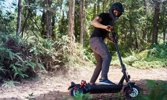 Un homme en casque roule en trottinette électrique dans une forêt. Il semble rencontrer un problème, peut-être un code erreur e8 trottinette électrique.
