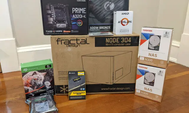 Composants pour installer un NAS : carte mère ASUS, processeur AMD Athlon, boîtier Fractal Design, alimentation, RAM Corsair, et deux disques durs Toshiba 8 To.