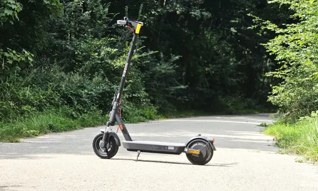 Trottinette Xiaomi grise sur une route asphaltée, entourée de verdure. Parfait pour explorer la nature et profiter de son autonomie.